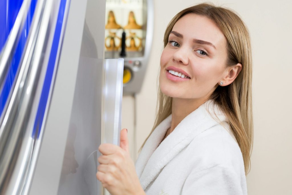 Portrait of happy girl in white robe in Solarium. Cosmetology. Vertical Solarium